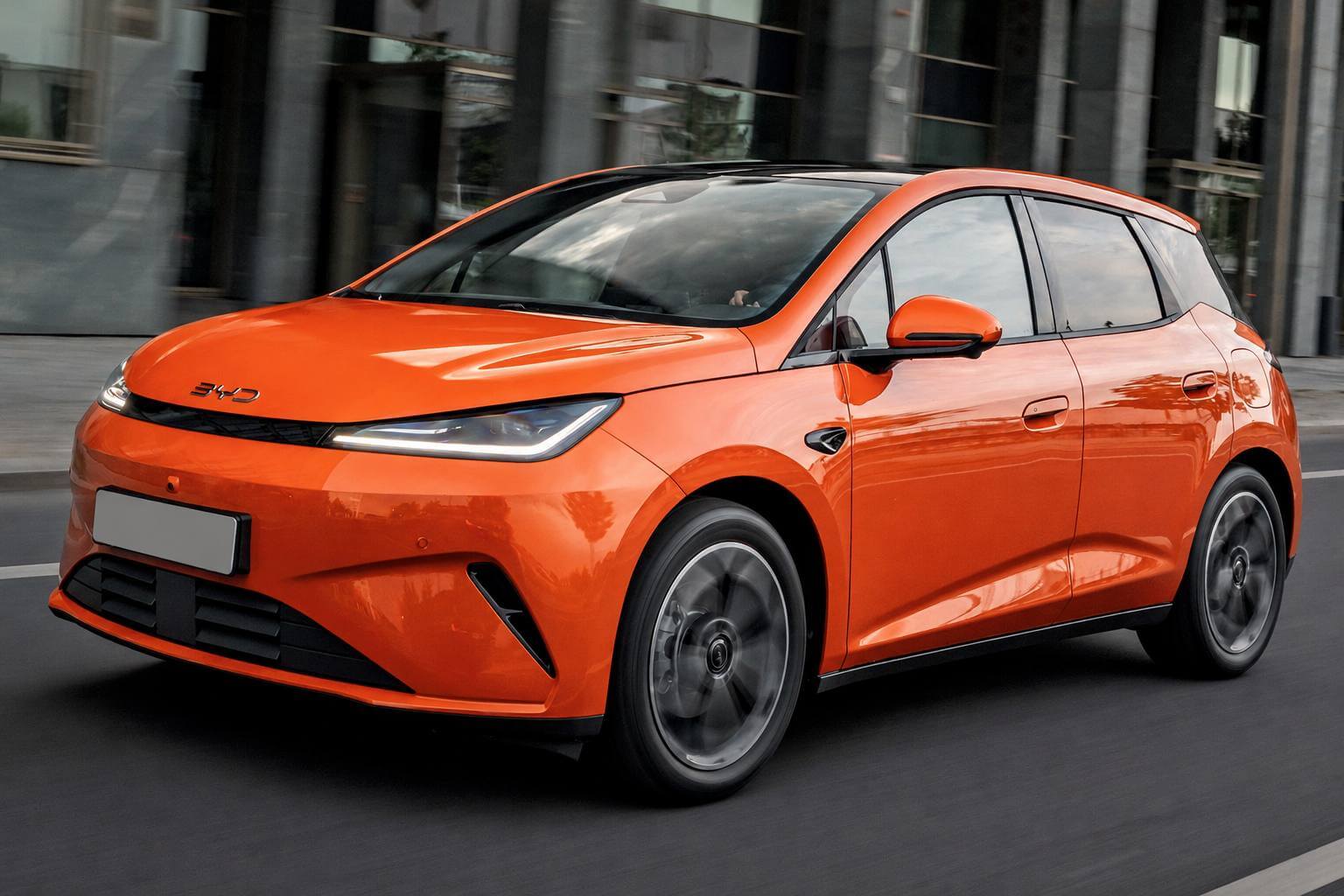 BYD Dolphin G Sport laranja visto de frente em três quartos, em movimento numa rua urbana