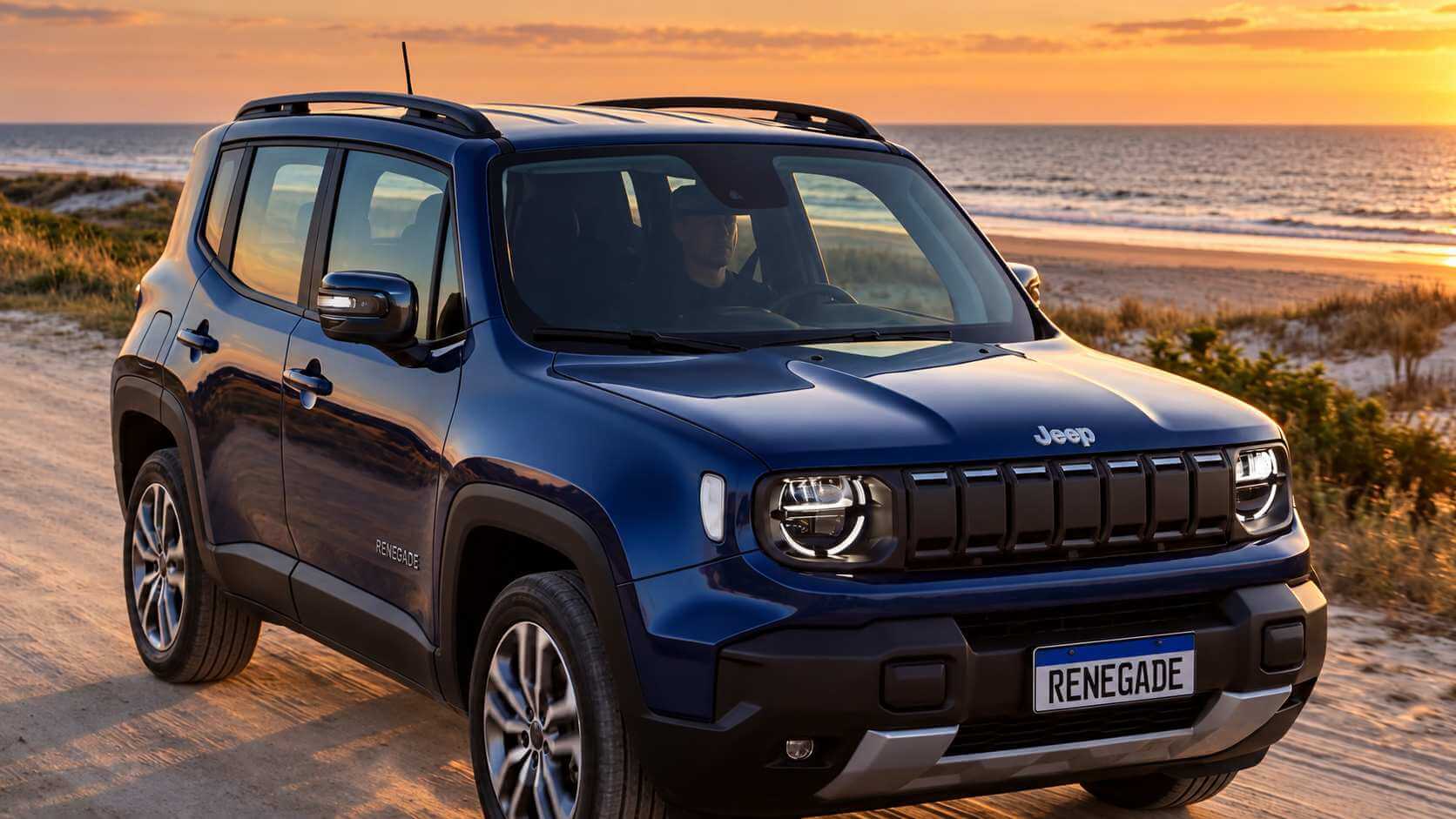 Jeep Renegade azul-escuro visto de frente em três quartos, parado em uma estrada de areia à beira da praia no fim da tarde, com o mar e o céu alaranjado ao fundo. Aparecem a grade de sete fendas, o nome Jeep no capô, o letreiro RENEGADE na lateral e a placa dianteira com o nome RENEGADE.