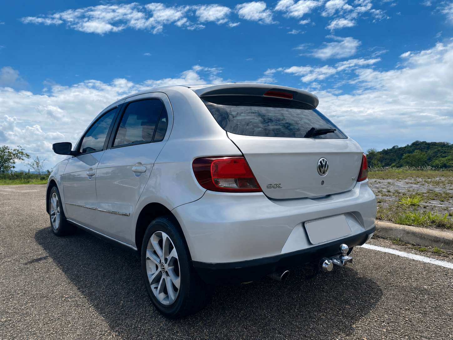 Volkswagen Gol G5 Power 1.6 prata, hatch visto de traseira em três quartos, parado numa estrada de campo com céu azul e colinas ao fundo; aparecem o emblema VW, a inscrição GOL, o badge 1.6 e rodas de liga leve.