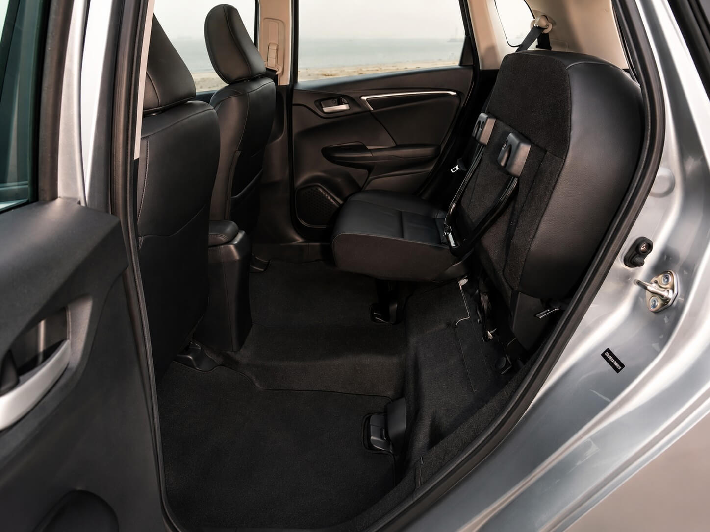 Interior traseiro do Honda Fit com o Magic Seat acionado: o assento traseiro levantado na vertical contra o encosto, revelando o piso plano e um grande espaco de carga atras dos bancos dianteiros.