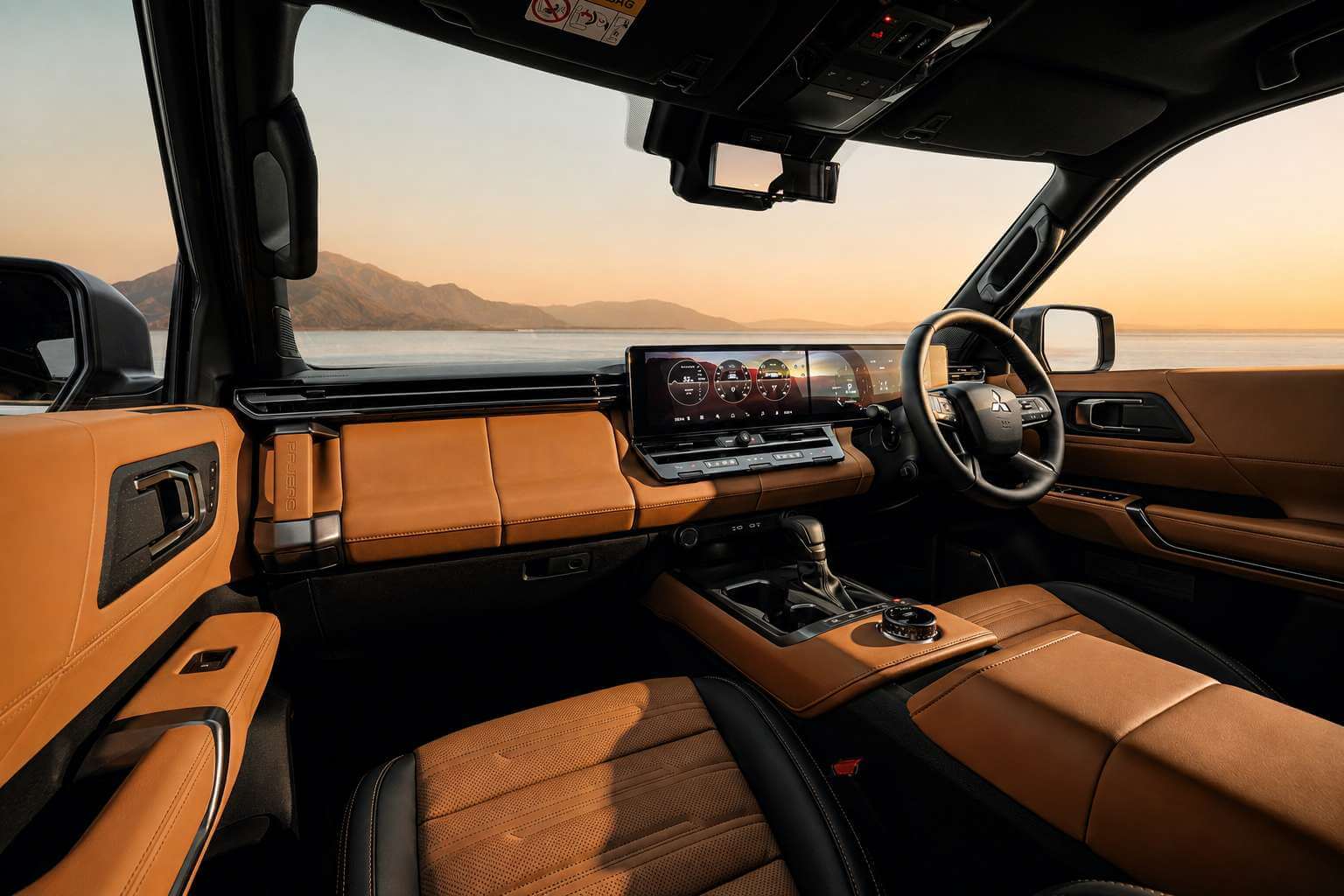 Painel do novo Mitsubishi Pajero 2027 visto do banco do passageiro: duas telas de 14,3 polegadas conjugadas em um unico painel de vidro, com instrumentos digitais e mapa; abaixo delas, uma fileira de botoes fisicos e saidas de ar. O acabamento e em couro caramelo com costura aparente, a alavanca de cambio fica no console central ao lado do seletor circular de modos de conducao, e o volante, a direita, traz o emblema de tres diamantes da Mitsubishi. Pelo para-brisa aparecem montanhas e um lago sob luz dourada de fim de tarde.