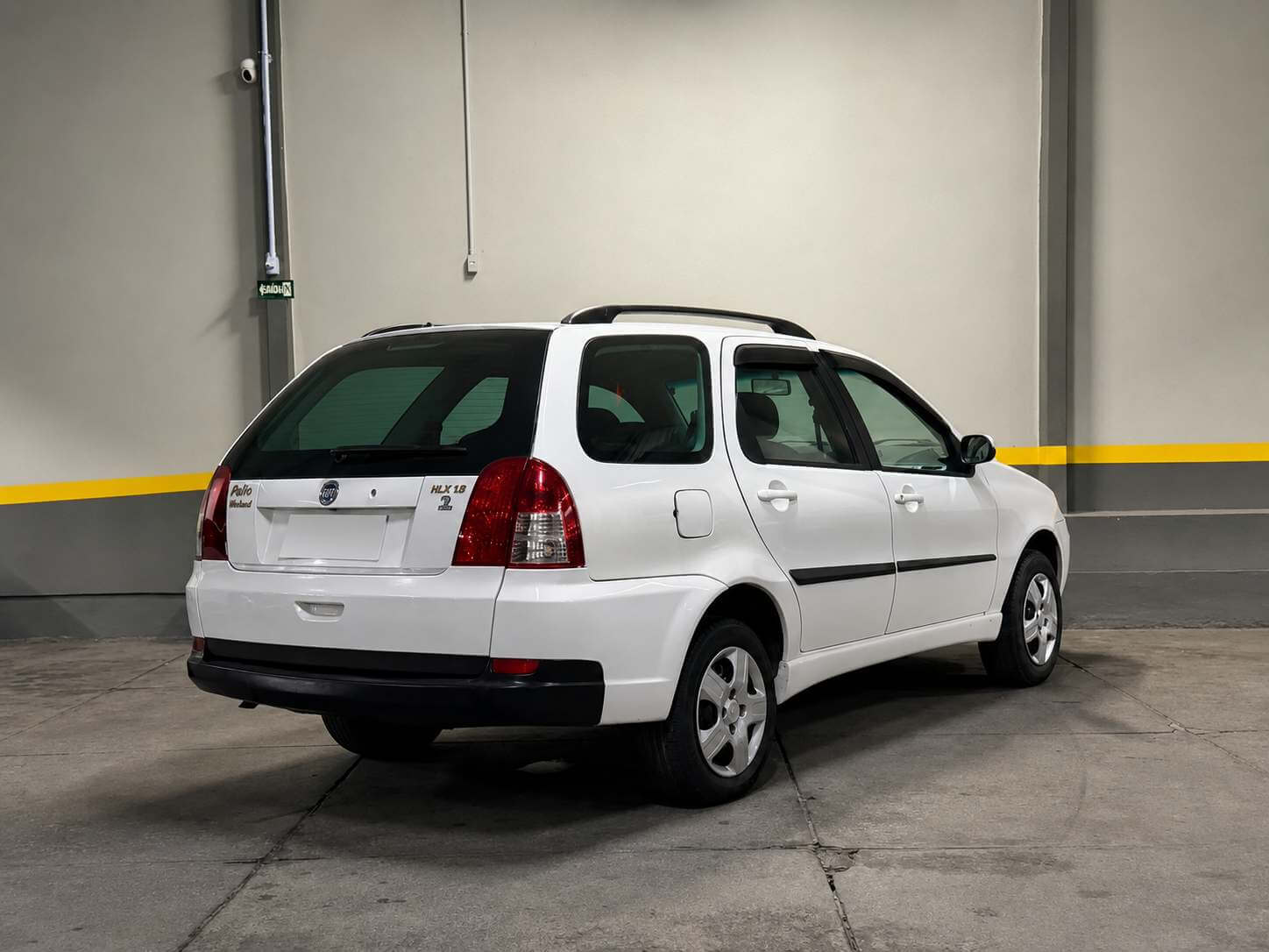 Fiat Palio Weekend HLX 1.8 branca, vista de traseira em três quartos numa concessionária, com barras longitudinais no teto, rodas de liga leve e, na tampa traseira, o emblema da Fiat e as inscrições Palio Weekend e HLX 1.8.
