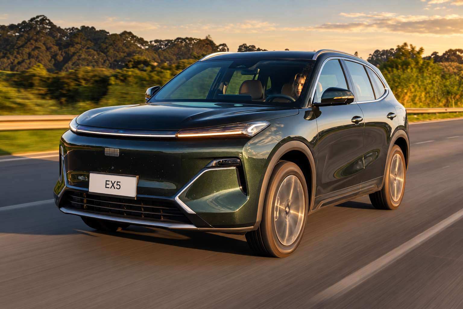 Geely EX5 EM-i Ultra 2027 na cor verde-escura, vista de tres quartos dianteira, rodando por uma rodovia arborizada sob luz de fim de tarde. O SUV hibrido plug-in aparece em movimento, com faixa de LED atravessando a dianteira, grade fechada com o emblema Geely no centro, rodas de liga leve de acabamento dourado, barras longitudinais no teto e placa dianteira escrita EX5.