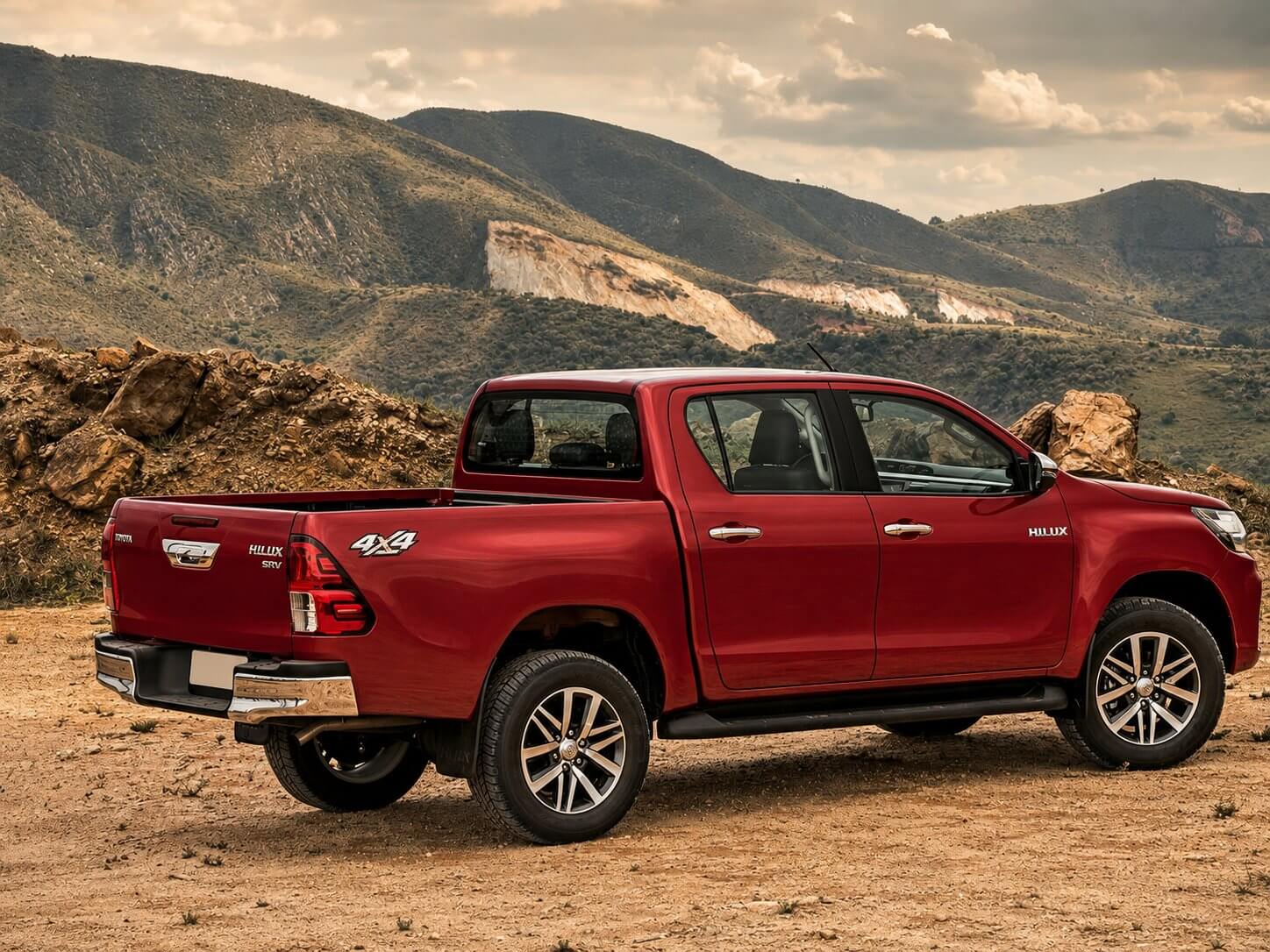 Toyota Hilux SRV 4x4 vermelha vista em três quartos traseiro numa estrada de terra com montanhas ao fundo; picape média de cabine dupla com o emblema da Toyota e as inscrições Hilux, SRV e 4x4 na carroceria.