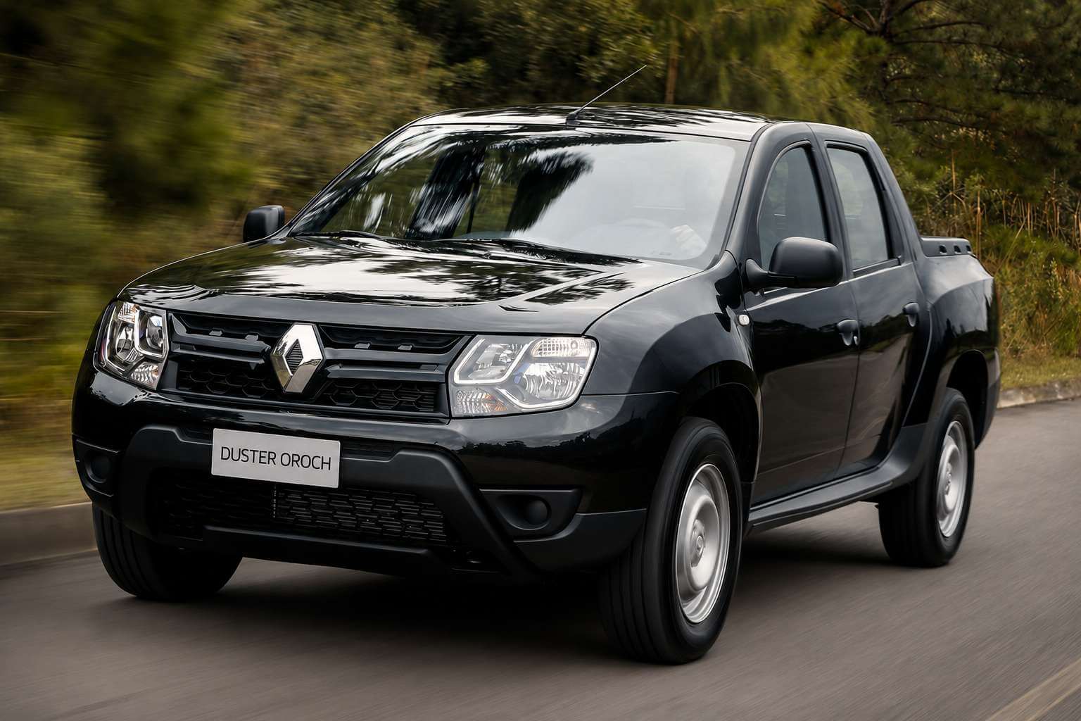Renault Duster Oroch Expression 2017 na cor preta, picape de cabine dupla com quatro portas, vista em três quartos dianteira enquanto roda por uma estrada de asfalto cercada de mata verde; as rodas de liga leve de 16 polegadas aparecem borradas pelo movimento e a placa dianteira mostra apenas o nome do modelo