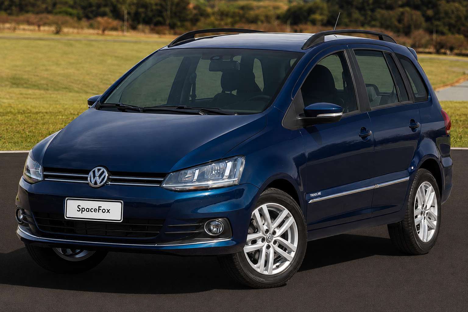 Volkswagen SpaceFox Trendline azul-escuro metalico da fase final, linha 2017 a 2019, fotografada parada de tres quartos dianteiros sobre uma pista de asfalto, com um campo de grama seca e arvores desfocadas ao fundo sob luz forte de fim de tarde. A perua mostra a dianteira da segunda reestilizacao: capo mais alto, farois quadrados e inclinados, friso cromado horizontal atravessando a grade escura com o emblema da Volkswagen no centro, para-choque na cor da carroceria com faroletes de neblina circulares e placa dianteira branca escrita apenas SpaceFox. Na lateral aparecem o badge TRENDLINE no para-lama, o friso cromado ao longo das portas, as barras longitudinais pretas no teto, retrovisores na cor do carro e rodas de liga leve de cinco raios duplos com pneus de perfil alto.