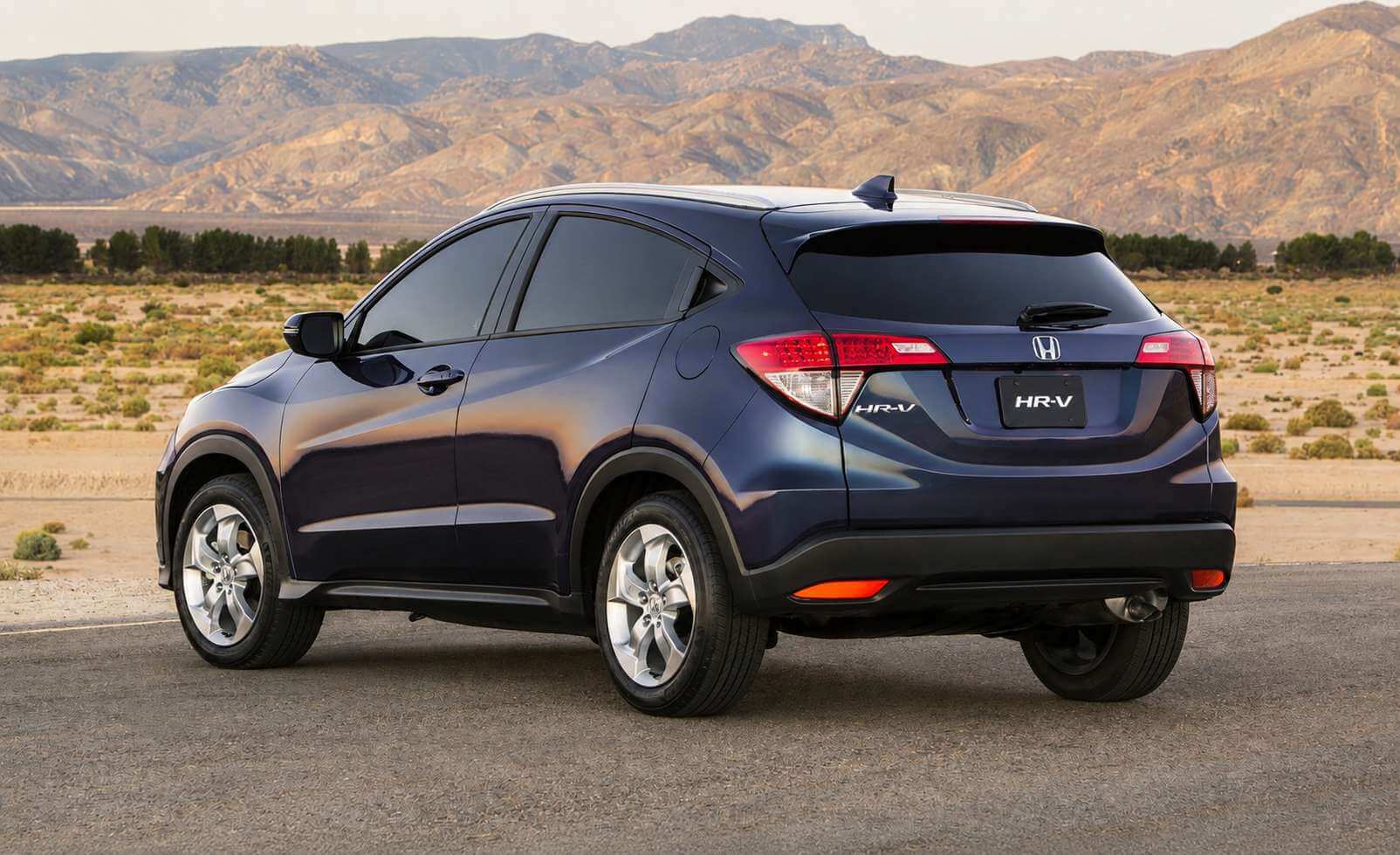 Honda HR-V EXL de primeira geração na cor azul-escuro metálico, visto em três quartos traseiro numa estrada de deserto com montanhas ao fundo; aparecem as lanternas traseiras alongadas, o emblema Honda e a inscrição HR-V na tampa e as rodas de liga diamantadas.