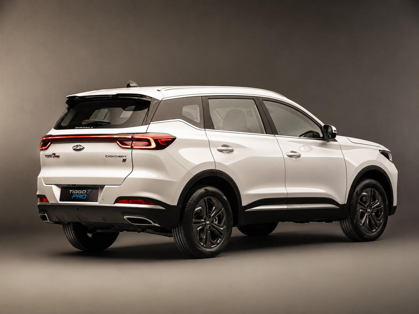 Caoa Chery Tiggo 7 Pro Max branca vista em três quartos traseiro, SUV médio com lanterna de LED em barra, o emblema da Chery e as inscrições Tiggo 7 Pro e Caoa Chery na tampa, rodas de liga escuras.
