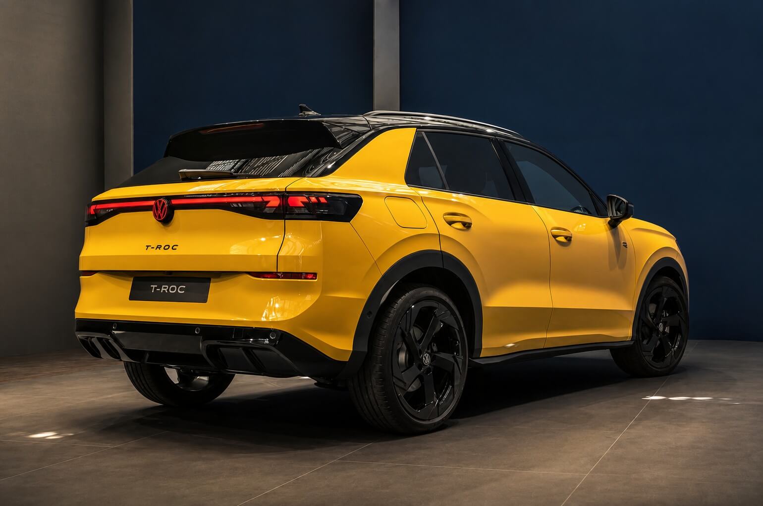 Volkswagen T-Roc 2026 R-Line na cor amarela, SUV compacto visto de tres quartos traseiro num estudio de fundo azul, com faixa de LED de ponta a ponta, emblema VW e lettering T-ROC na tampa e rodas de liga escuras.